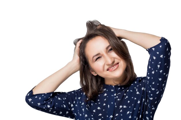 La bella ragazza castana in camicetta blu si diverte a scherzare con due mani solleva l'isolato orizzontale bianco del fondo del copyspace dei capelli