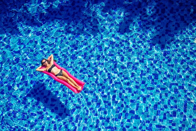 Beautiful brunette girl floating on mattresses in the pool.fitness female model in black bikini resting at hotel swimmingpool.diet, sport and bodybuilding concept water aerobics.