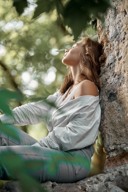 Bella ragazza bruna in jeans e una camicia bianca in posa sulle rovine nella foresta