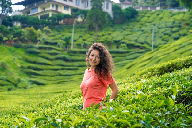 Beautiful brunette girl posing in the middle of the tea valley between green tea bushes.