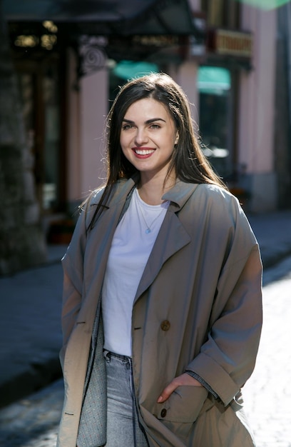 Bella ragazza bruna sorridente mentre si sta in piedi sulla strada soleggiata di primavera