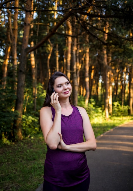 Bella ragazza castana parla al telefono nel parco al tramonto