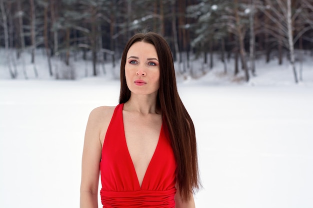 Beautiful brunette girl in a thin red dress and barefoot in the winter forest