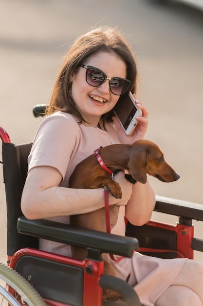 Beautiful brunette girl in a wheelchair in summer on a walk with a cute dog