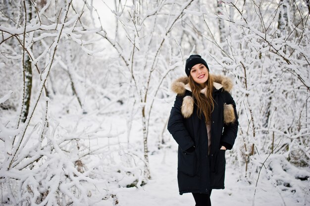 Beautiful brunette girl in winter warm clothing. Model on winter jacket and black hat.