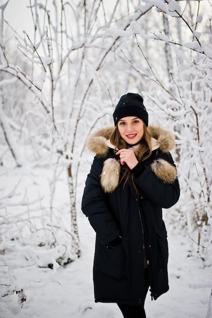 Beautiful brunette girl in winter warm clothing. Model on winter jacket and black hat.