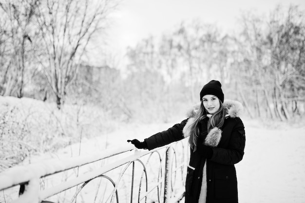 Beautiful brunette girl in winter warm clothing. Model on winter jacket and black hat.