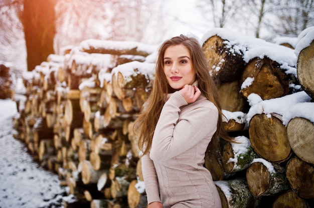 Beautiful brunette girl in winter warm clothing. Model on winter sweater near stump.