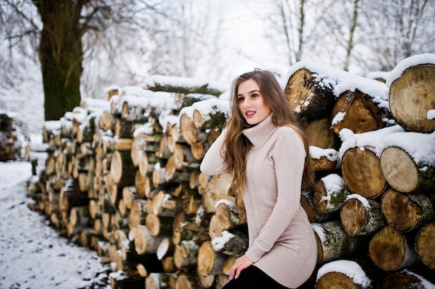 Beautiful brunette girl in winter warm clothing. Model on winter sweater near stump.