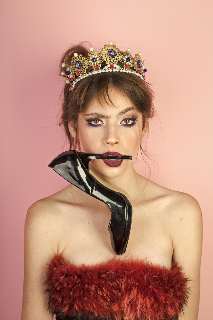 Photo beautiful brunette girl with a golden crown and professional evening makeup beauty face with shoe in mouth