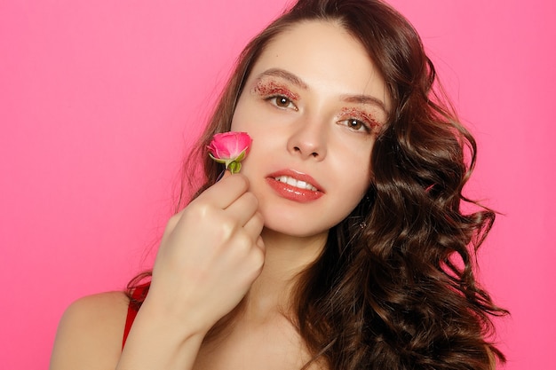 Beautiful brunette girl with green eyes make up and fresh skin posing at pink background with flower, skin care concept, beauty spa, bio product. Horizontal