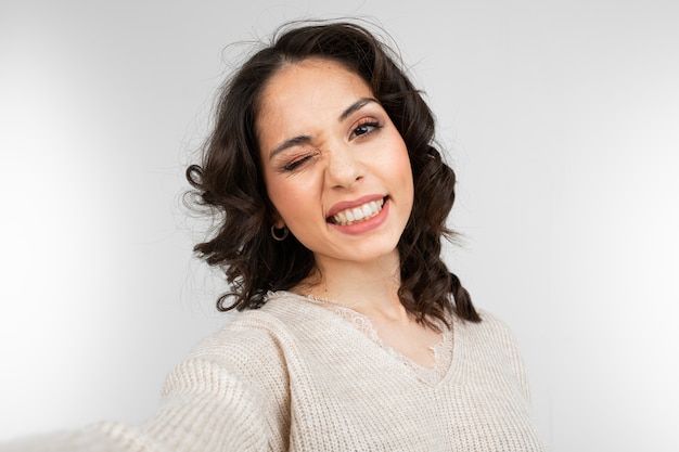 beautiful brunette girl with makeup makes selfie while grimacing on gray studio