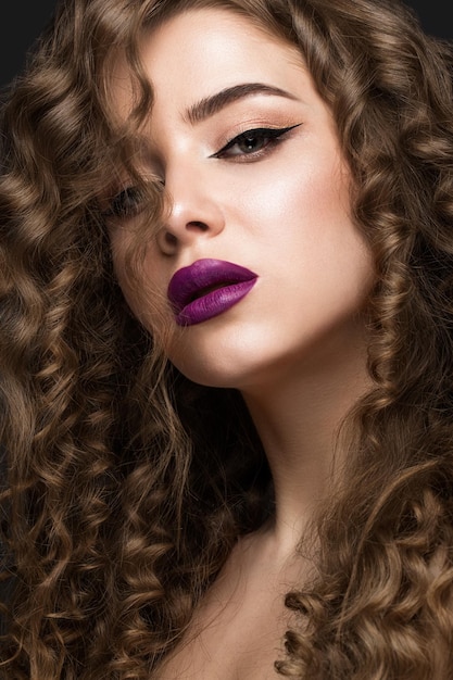 Beautiful brunette girl with a perfectly curly hair and classic makeup Beauty face