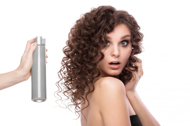 Bella ragazza bruna con i capelli perfettamente ricci con flacone spray e trucco classico. volto di bellezza.