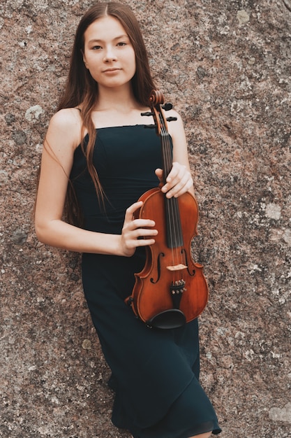 Beautiful brunette girl with violin at the rock. High quality photo