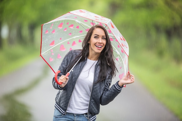 美しいブルネットは雨の日にカメラに微笑んで傘の下に隠れています。