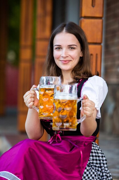 Photo the beautiful brunette holds 2 pints of beer at the oktoberfest in germany