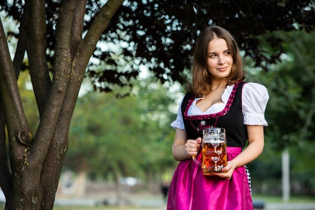 Photo the beautiful brunette holds 2 pints of beer at the oktoberfest in germany
