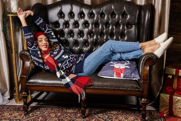 A beautiful brunette lies in a leather armchair against the backdrop of Christmas decorations