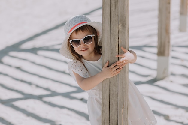 夏のビーチで遊ぶ白いドレスと帽子の美しいブルネットの少女