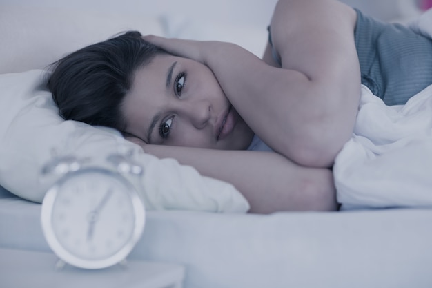 Beautiful brunette looking at alarm clock in her bed