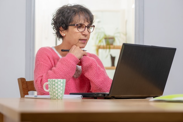 Beautiful brunette mature woman dressed in pink with laptop at home