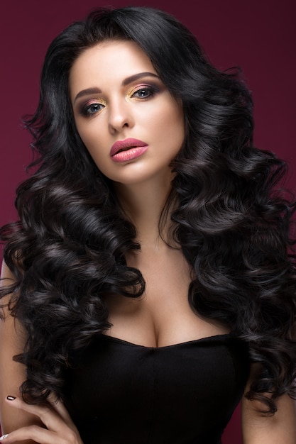Beautiful brunette model: curls, classic makeup, gold jewelry and red lips. The beauty face.