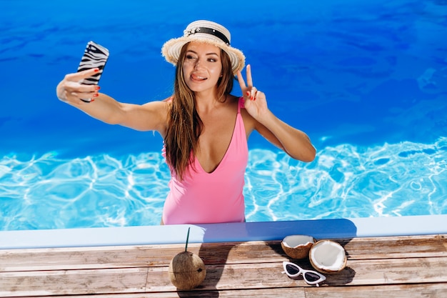 Beautiful brunette in pink swimsuit posing by the pool