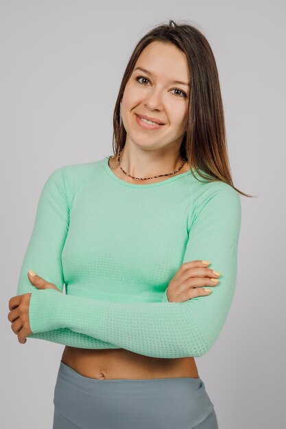 Beautiful brunette posing Portrait of happy young woman in tracksuit for yoga or fitness posing in studio on gray isolated background she crossed her arms and tilted her head