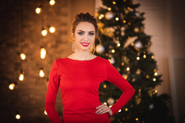 Beautiful brunette in a red dress on the background of the Christmas tree.