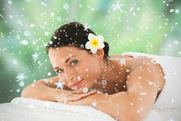 Beautiful brunette relaxing on massage table smiling at camera against snow