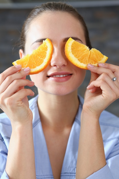 La bella donna sorridente castana mangia l'arancia affettata