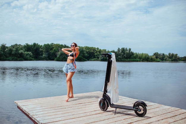 A beautiful brunette in a swimsuit sunbathes on a wooden bridge and there is a scooter nearby. Ecology and health care concept. High quality photo