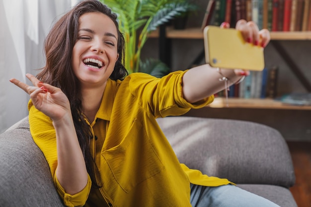 Beautiful brunette taking selfie with her smartphone at home