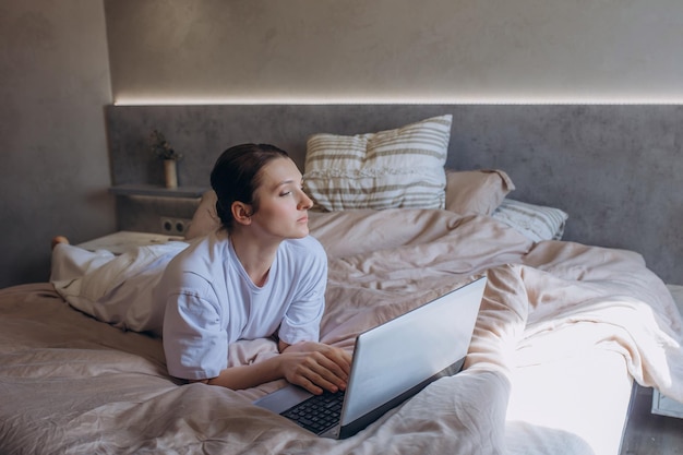A beautiful brunette woman in the bedroom on the bed working with a laptop
