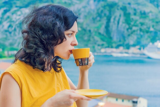 Foto una bella donna bruna beve caffè da una tazza gialla sullo sfondo del mare