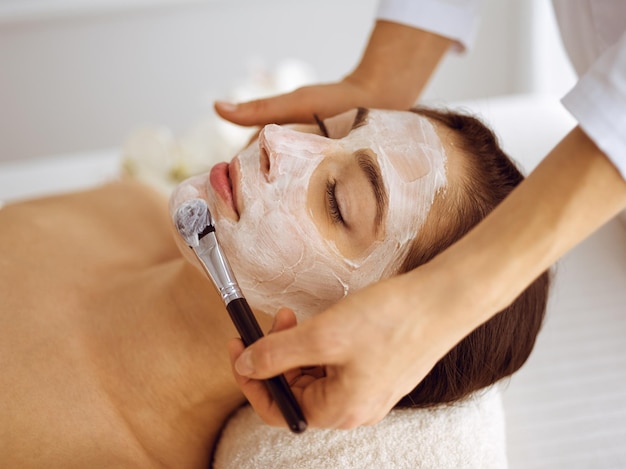 Photo beautiful brunette woman enjoying applying cosmetic mask with closed eyes. relaxing treatment in medicine and spa center concepts.
