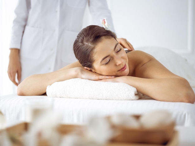 Beautiful brunette woman enjoying back massage with closed eyes. Spa and medicine concept.