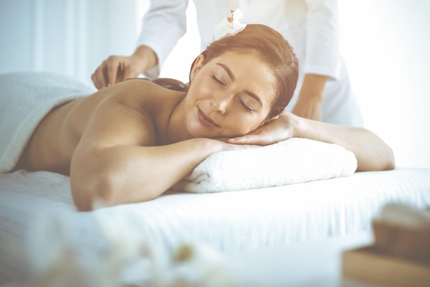 Beautiful brunette woman enjoying back massage with closed eyes. Spa and medicine concept