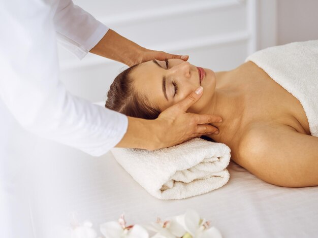 Beautiful brunette woman enjoying facial massage with closed eyes. Relaxing treatment in medicine and spa center concepts.