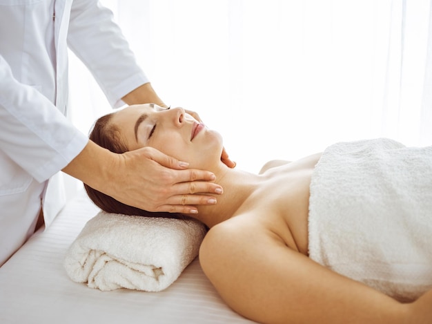 Photo beautiful brunette woman enjoying facial massage with closed eyes. relaxing treatment in medicine and spa center concepts.