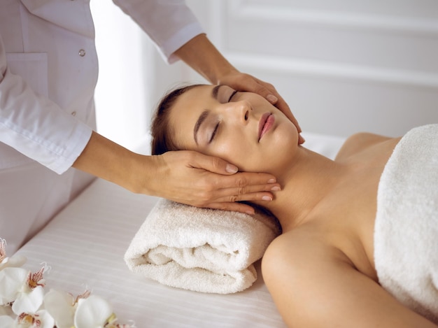 Beautiful brunette woman enjoying facial massage with closed eyes. Relaxing treatment in medicine and spa center concepts.