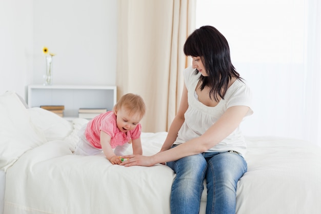 Beautiful brunette woman enjoying a moment with her baby while sitting on a bed