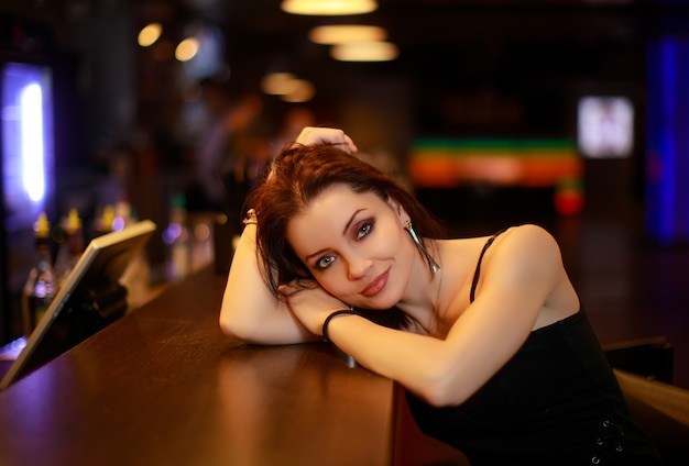 Красивая брюнетка женщина в вечернем платье позирует возле бара в одиночестве