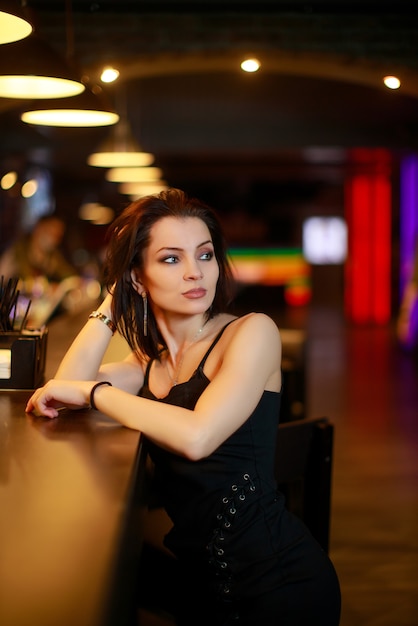 Beautiful brunette woman in evening dress posing near bar alone