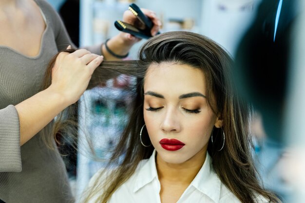 Beautiful brunette woman has hair iron in beauty salon