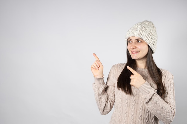 Beautiful brunette woman in a hat and sweater points her fingers at a place for text