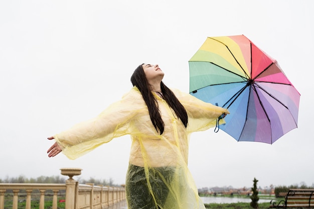 カラフルな傘を持った美しいブルネットの女性が雨滴をキャッチし、雨を楽しんでいます。