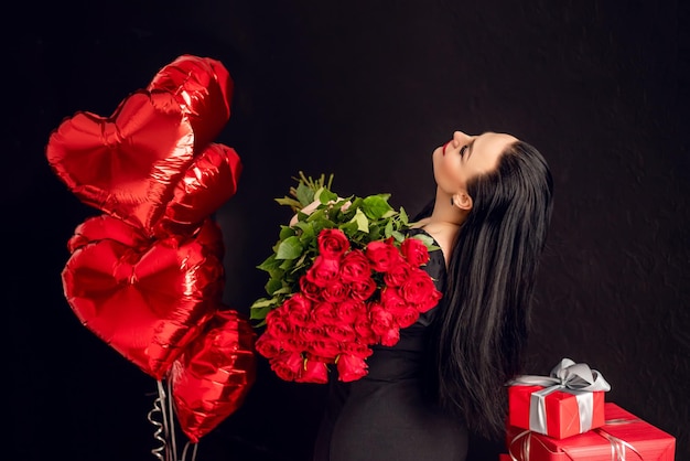 beautiful brunette woman holds a large bouquet of red roses against a background of red balls