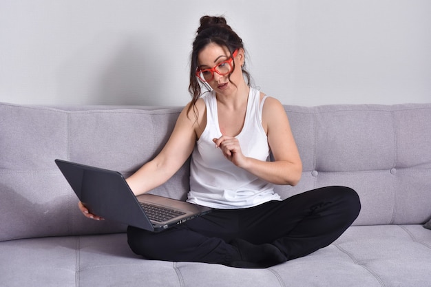 Фото Красивая брюнетка женщина в красных очках на диване, используя ноутбук